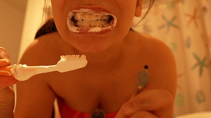 A giantess brushes her teeth while her tiny husband watches.